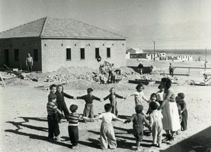 בונים באילת (שכונה א') גן ילדים ראשון - בתמונה הילדים והגננת רוקדים בחזית הגן. (הצילום באדיבות מוזיאון "אילת עירי")